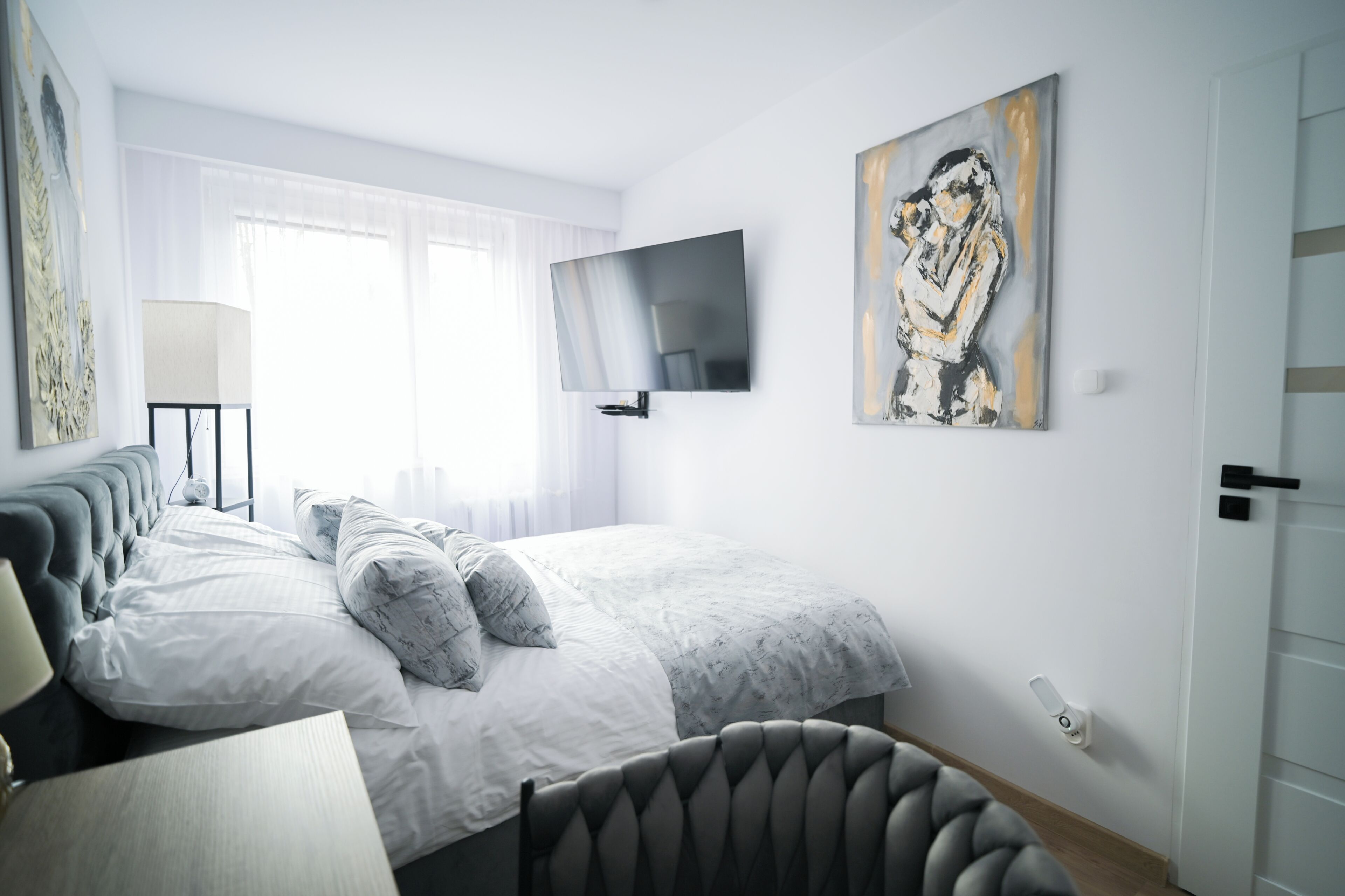 Een moderne slaapkamer met een bed, een flatscreen televisie, een schilderij en een lamp.