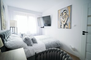 A modern bedroom with a bed, a flat-screen TV, a painting, and a lamp.