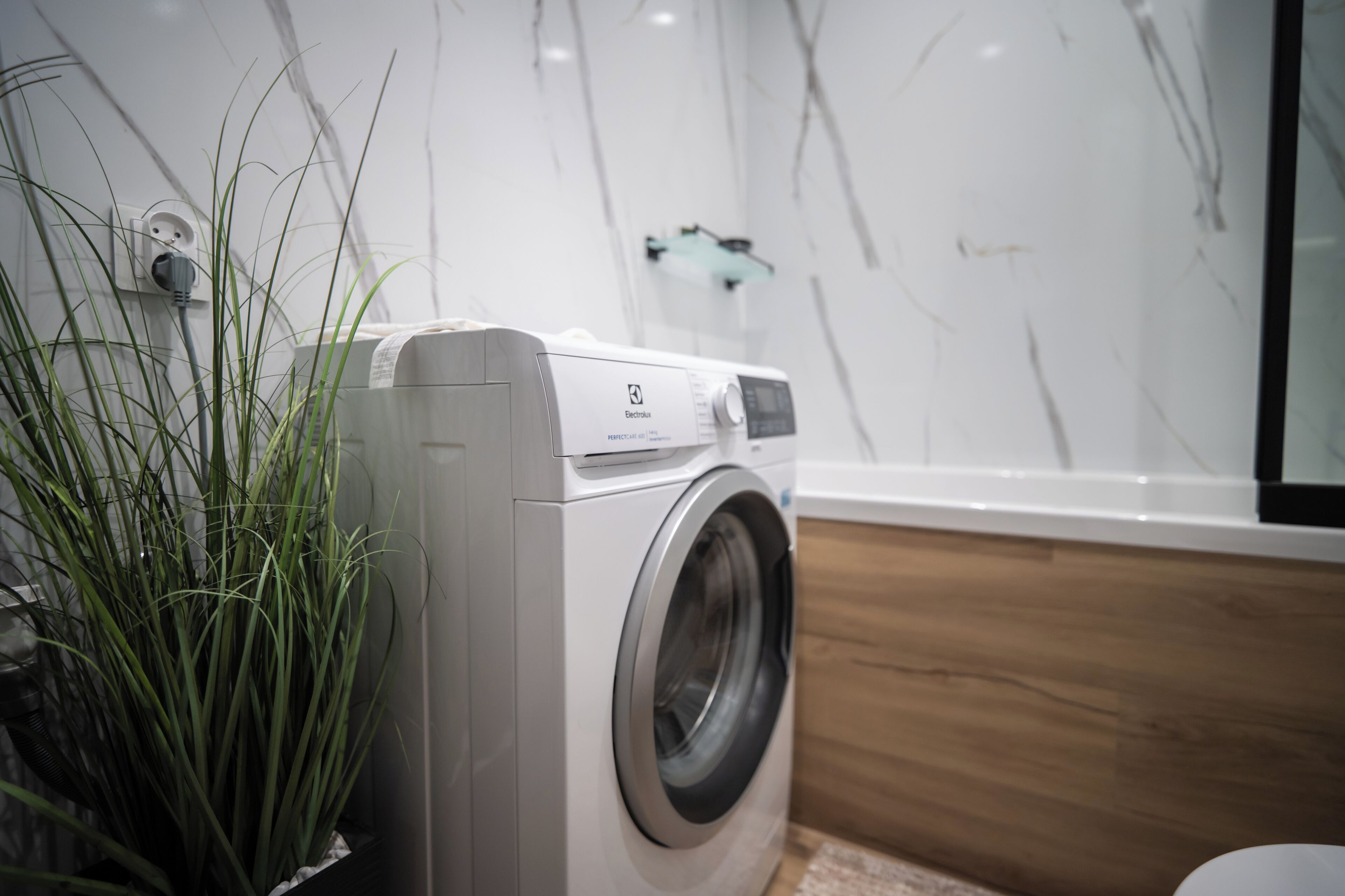 Een voorlader wasmachine in een moderne badkamer met een marmeren wand en een houten vloer.