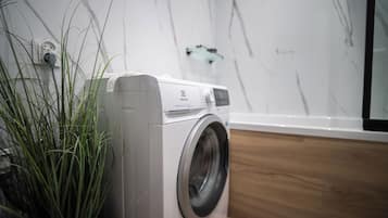 Een voorlader wasmachine in een moderne badkamer met een marmeren wand en een houten vloer.