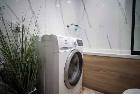 A front-loading washing machine in a modern bathroom with a marble wall and a wooden floor.