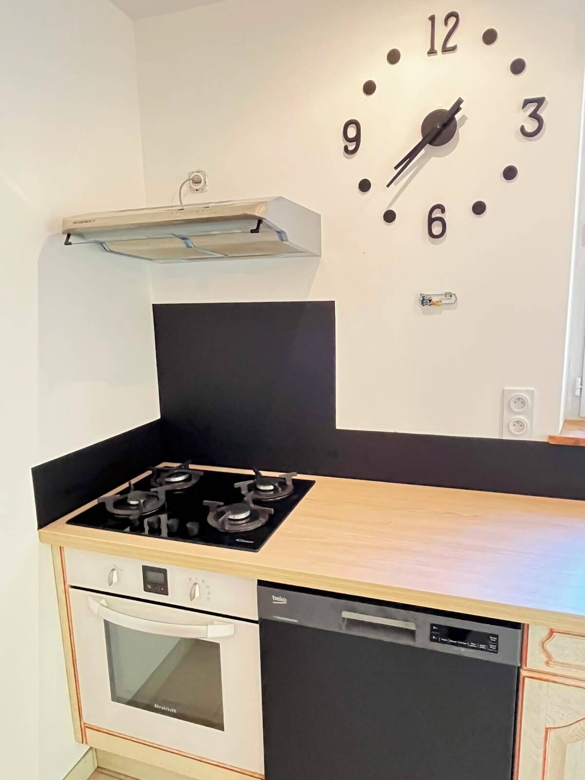A kitchen with a stove, oven, and dishwasher, a clock on the wall, and a hanging light fixture.