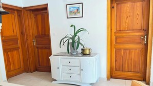 Quarto com um armário branco, uma mesa e uma cadeira. Há uma porta de madeira e um quadro na parede.