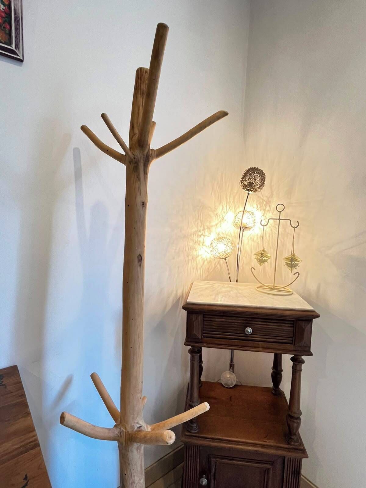 Un perchero de madera con ramas y una mesita con una lámpara.
