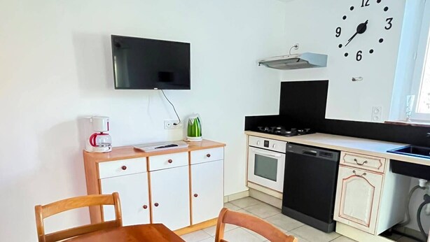 Uma cozinha com uma mesa de jantar, cadeiras, uma televisão na parede e um relógio.