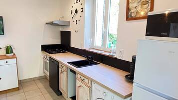 Cocina compacta con pileta, estufa y lavavajillas. Se ve un reloj en la pared y una ventana que proporciona luz natural.