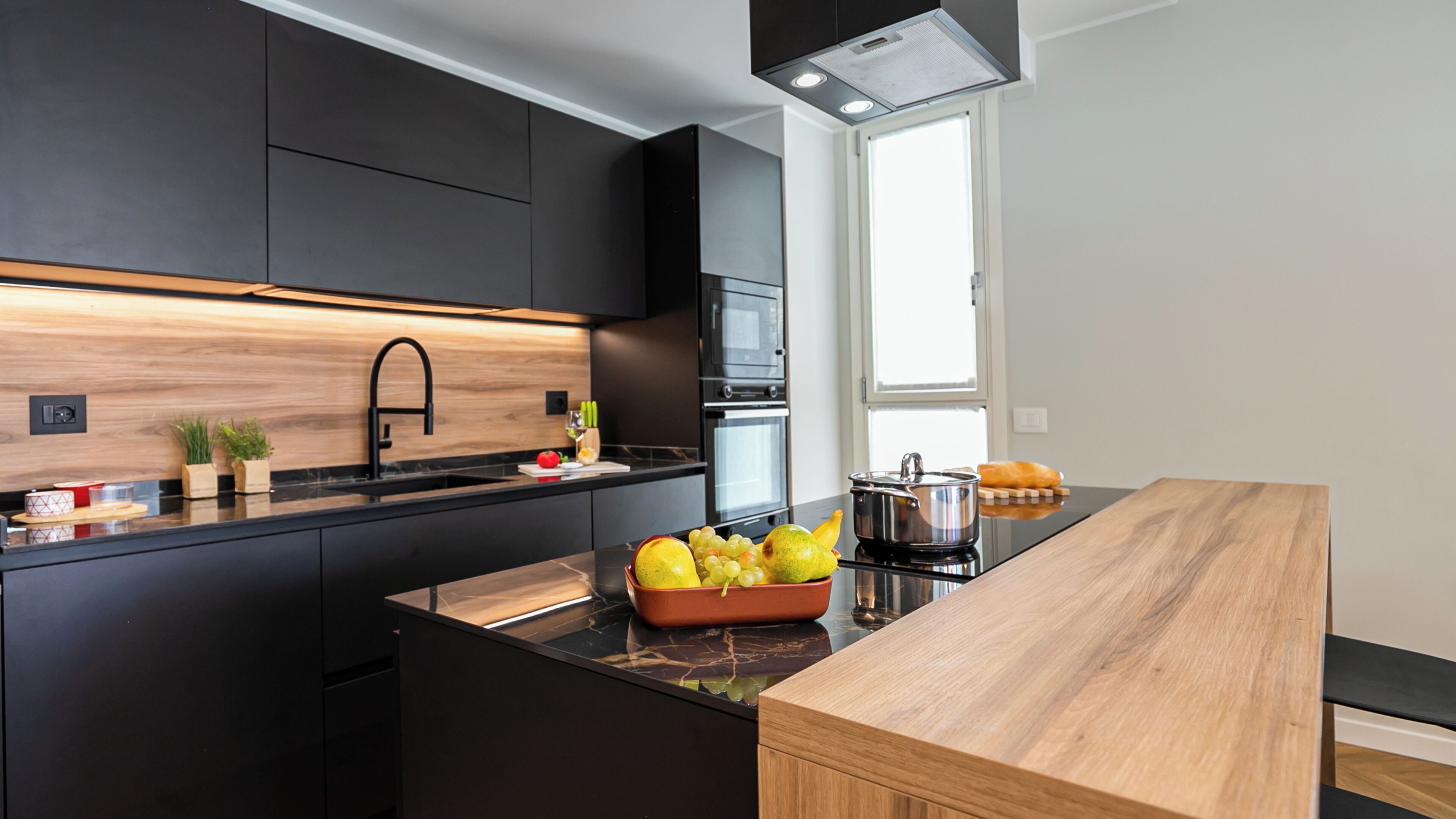 A modern kitchen with black cabinets, a wooden countertop, and a built-in oven.