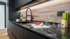Ett modernt kök med en svart bänkskiva, en diskho i rostfritt stål, en träpanel bakom diskbänken och ett vinglas i glas.