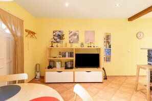 Una sala de estar con televisor, estanterías y una zona de comedor.