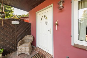 Una puerta blanca con un cartel de bienvenida, una silla de mimbre y un pequeño escalón que lleva a la entrada.