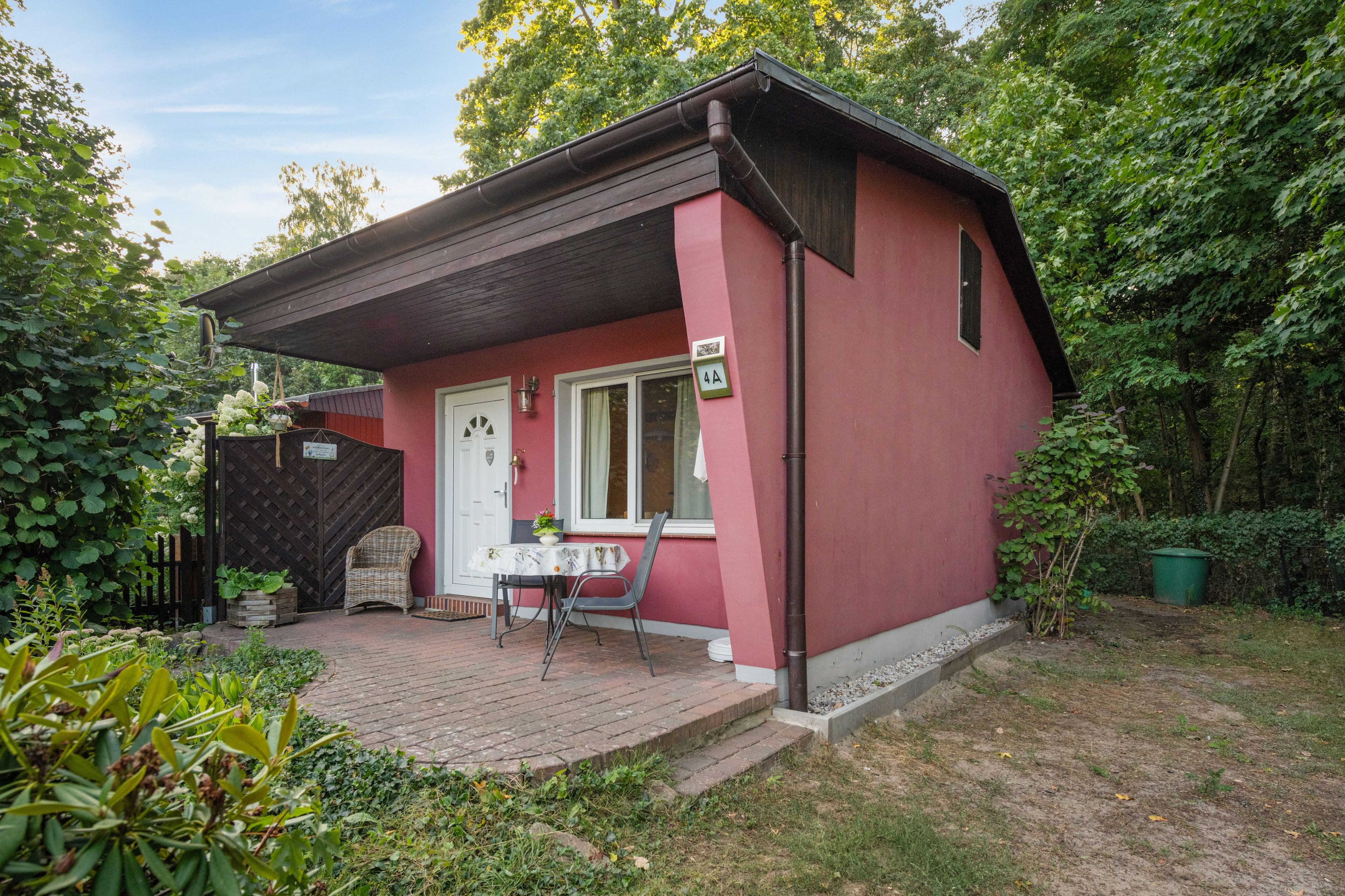 Ein kleines, eingeschossiges Gebäude mit roter Fassade, einer weißen Tür und einer kleinen Veranda mit Tisch und Stühlen.