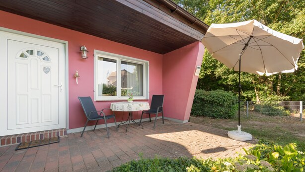 Un patio con una mesa, sillas, una puerta blanca y un paraguas grande.