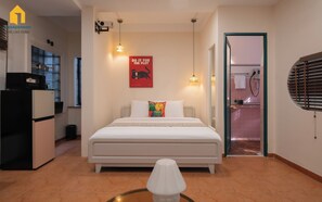 Una camera da letto con un letto, un tavolino, un proiettore a parete e un angolo cottura visibile attraverso una porta aperta.