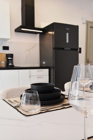 A modern kitchen with a black refrigerator, a coffee maker, and a dining table set with plates, glasses, and cutlery. - Luxury City Apartment, 3 bedrooms 3 bathrooms, Chania Center (Chania)
