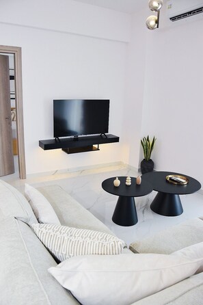 A modern living room with a flat-screen TV mounted on the wall, a round black coffee table with decorative items, and a sofa with patterned cushions. - Luxury City Apartment, 3 bedrooms 3 bathrooms, Chania Center (Chania)