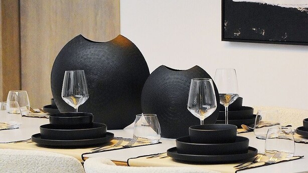 Uma sala de jantar com mesas redondas, cadeiras e vasos decorativos pretos.