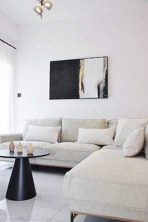 A modern living room with a sectional sofa, a round black coffee table, and a large abstract painting on the wall. - Luxury City Apartment, 3 bedrooms 3 bathrooms, Chania Center (Chania)