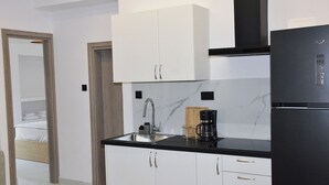 Cozinha compacta com armários brancos, bancada preta, cafeteira e geladeira.