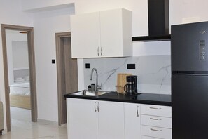 A compact kitchen with white cabinets, a black countertop, a coffee maker, and a refrigerator. - Luxury City Apartment, 3 bedrooms 3 bathrooms, Chania Center (Chania)