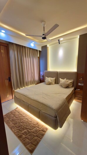 A modern bedroom with a large bed, a ceiling fan, recessed lighting, and a wooden door.