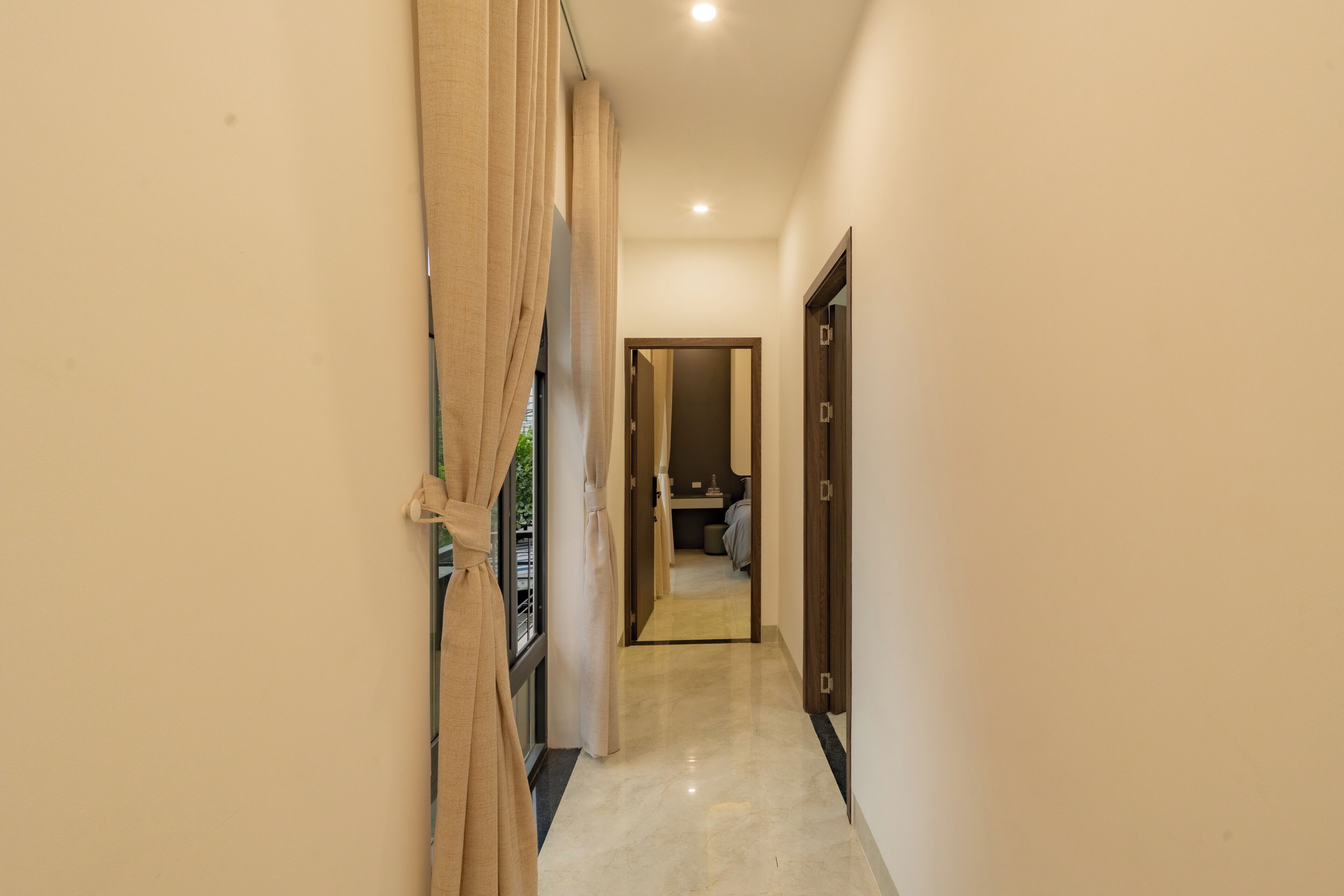 A corridor with a door at the end leading to a room with a bed and a small table.