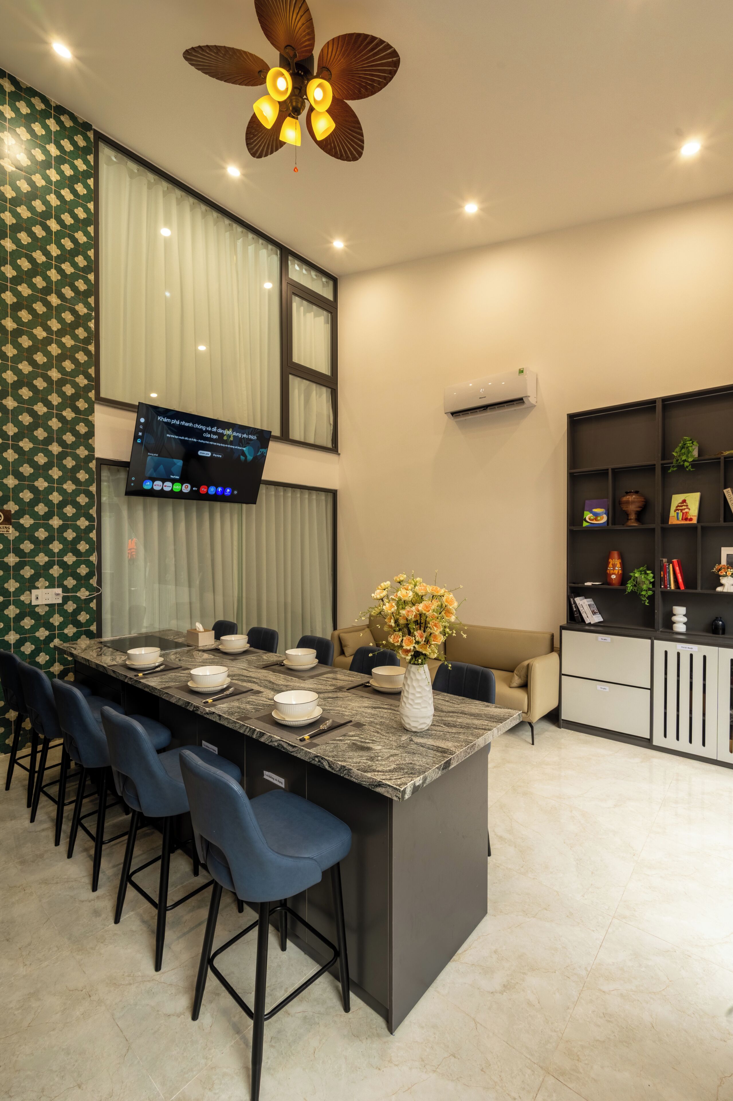 A modern kitchen with a central island, bar stools, a flat-screen TV, and a ceiling fan.