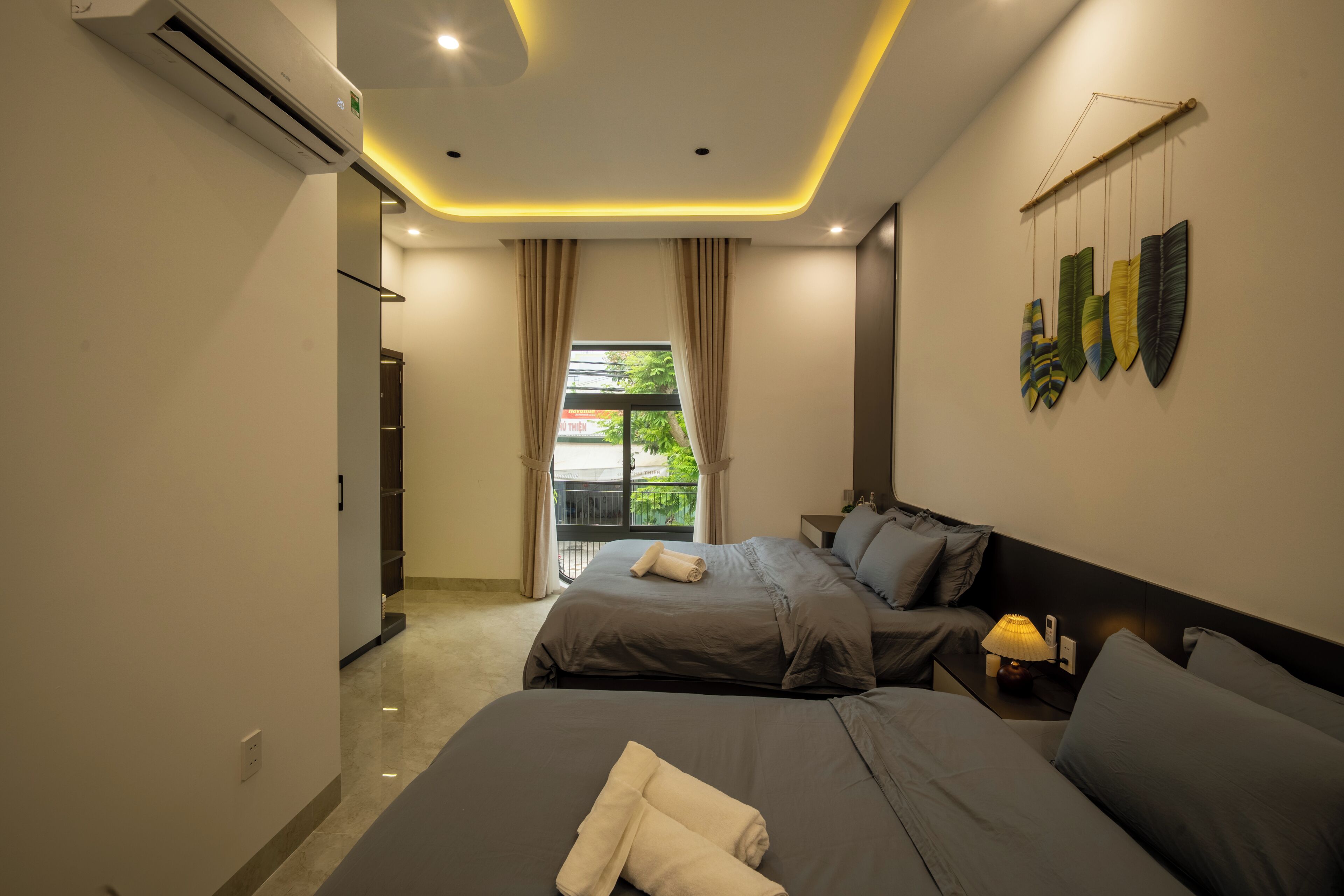 Un dormitorio moderno con dos camas, una mesita de noche, una lámpara y vistas al exterior.