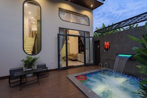 A modern outdoor pool area with a waterfall feature, a dining table with chairs, and a lounge chair. - H VILLA  (Da Nang)