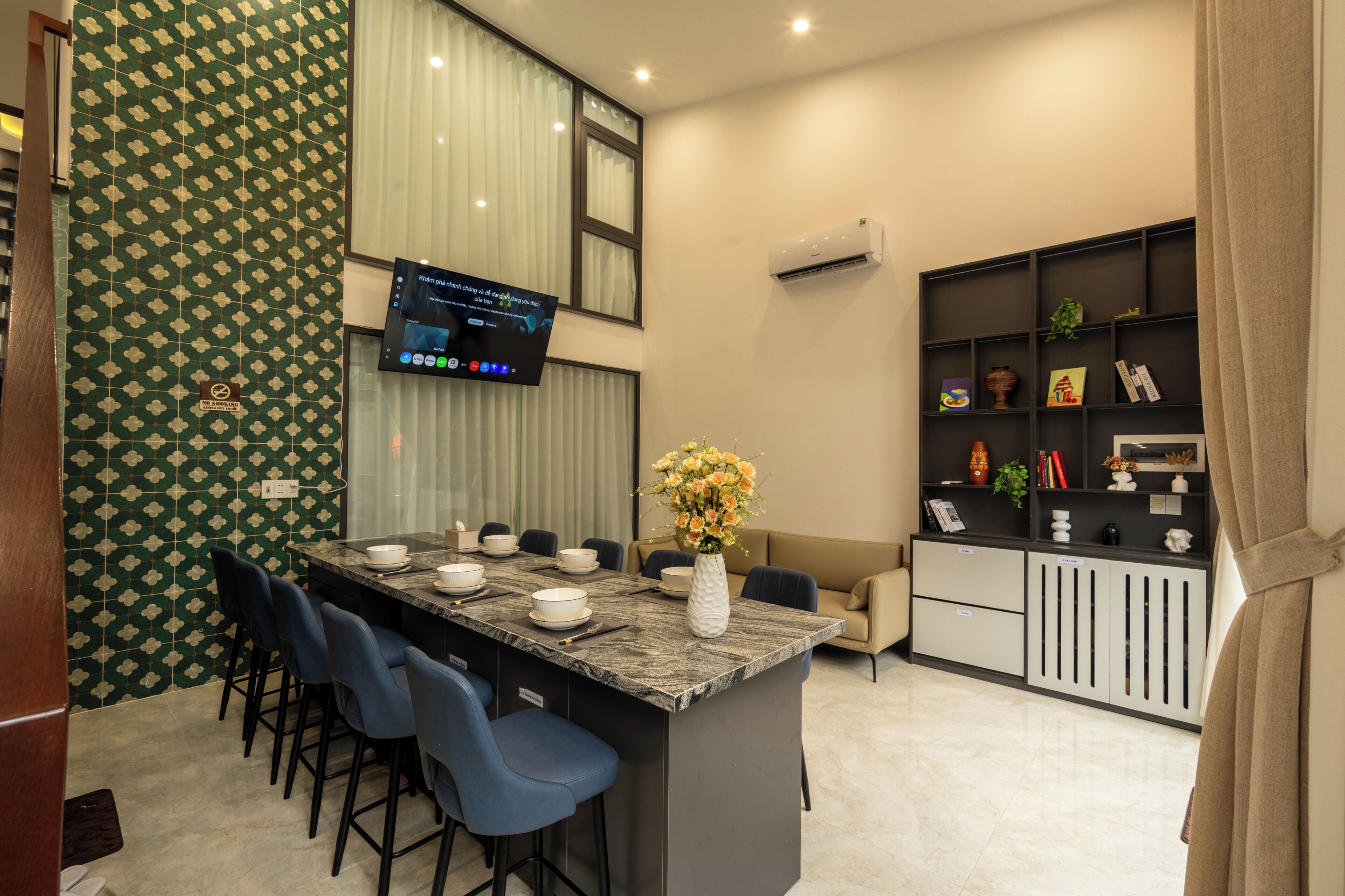 A modern kitchen with a central island, bar stools, a flat-screen TV, and a built-in bookshelf.