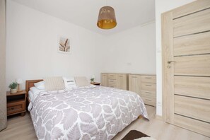 Een slaapkamer met een bed, nachtkastjes, een hanglamp, een deur en een aan de muur hangend schilderij.