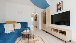 A modern living room with a blue sofa, a small round table with a plant, a large flat-screen TV, and a wooden entertainment unit. - Spacious Air-Conditioned Apartment | 2 Bedrooms | Workspace (Warszawa)