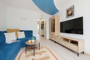 A modern living room with a blue sofa, a small round table with a plant, a large flat-screen TV, and a wooden entertainment unit. - Spacious Air-Conditioned Apartment | 2 Bedrooms | Workspace (Warszawa)