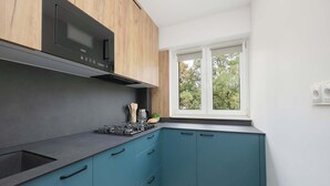 A modern kitchen with a built-in microwave, a gas stove, and teal cabinetry. - Spacious Air-Conditioned Apartment | 2 Bedrooms | Workspace (Warszawa)