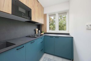 A modern kitchen with a built-in microwave, a gas stove, and teal cabinetry. - Spacious Air-Conditioned Apartment | 2 Bedrooms | Workspace (Warszawa)
