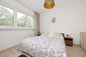 Een slaapkamer met een groot bed, een nachtkastje, een verwarming en een raam met gordijnen.