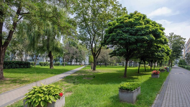 A park pathway lined with trees and planters with green foliage. - Spacious Air-Conditioned Apartment | 2 Bedrooms | Workspace (Warszawa)
