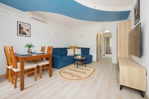 Een moderne woonkamer met een blauwe bank, een houten eettafel en een tv die aan een houten kast is bevestigd.