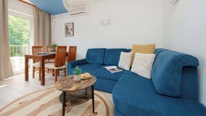 A living room with a blue sofa, a wooden dining table, and a small round coffee table. - Spacious Air-Conditioned Apartment | 2 Bedrooms | Workspace (Warszawa)