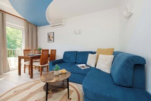 A living room with a blue sofa, a wooden dining table, and a small round coffee table. - Spacious Air-Conditioned Apartment | 2 Bedrooms | Workspace (Warszawa)