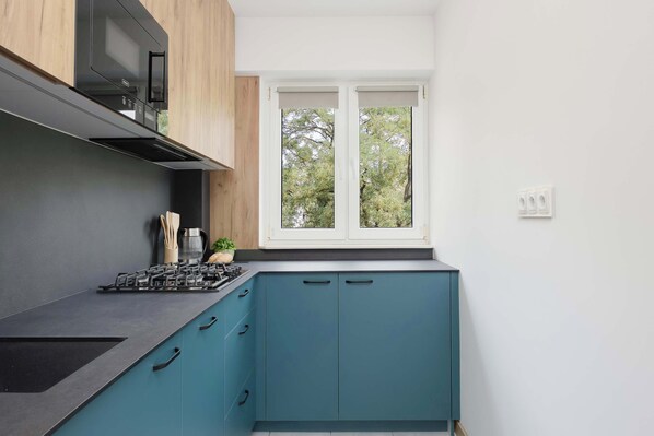 Een moderne keuken met een gasfornuis, kasten en een raam met uitzicht op bomen.