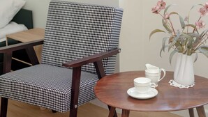 A houndstooth patterned armchair, a small round wooden table with a white pitcher, cup, and saucer, and a vase with pink flowers. - Cosy Studio in the Downtown in Gdansk by Noclegi Renters (Gdańsk)