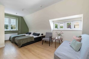 Ein Schlafzimmer mit zwei Betten, einem Sessel, einem kleinen Tisch und einem Fenster mit Blick auf Bäume.