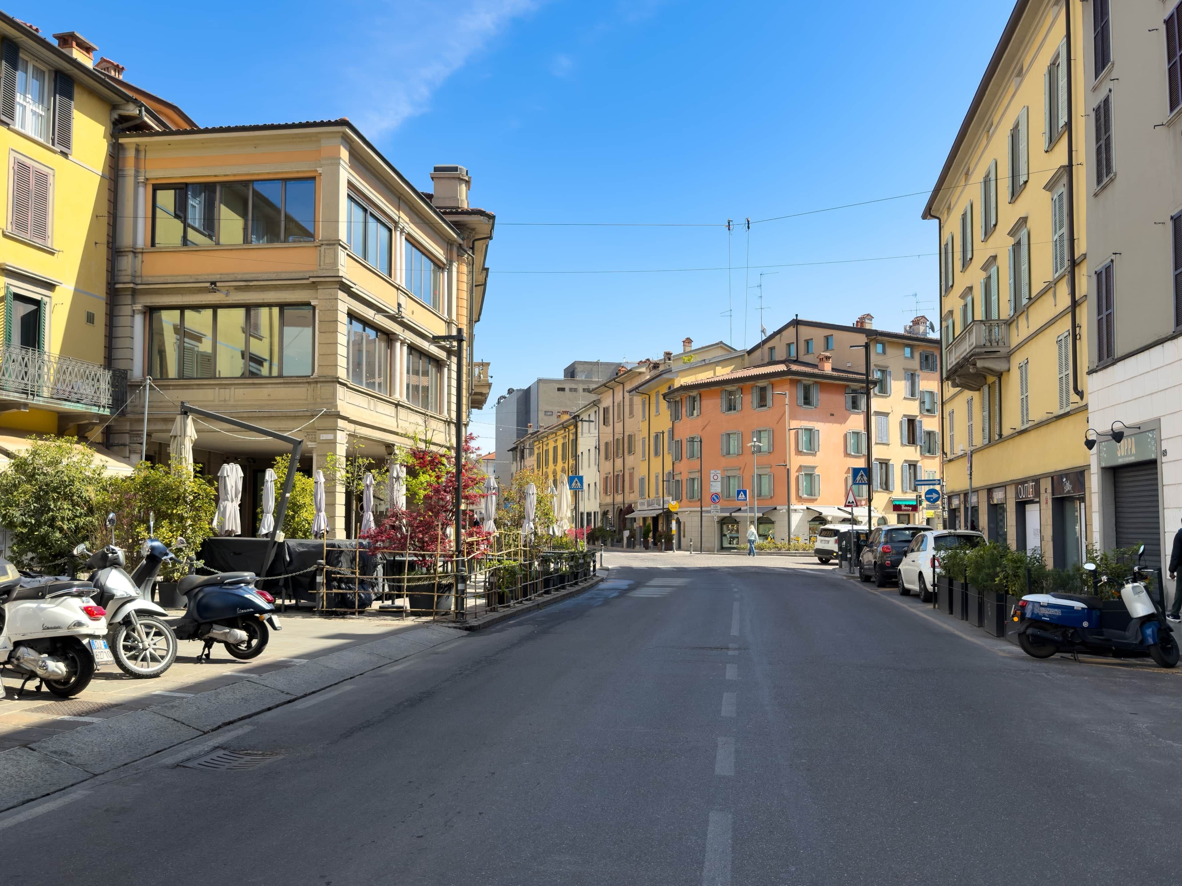 Eine Straße mit geparkten Rollern und Autos, Gebäude mit Balkonen und einem klaren Himmel.