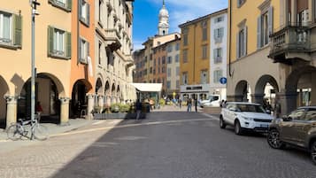Una strada acciottolata fiancheggiata da edifici storici, una torre dell'orologio e auto parcheggiate.