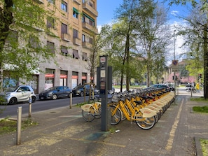 A row of yellow bicycles parked on a sidewalk, a row of parked cars, and a building with multiple windows and balconies. - Città Studi: Two-room apartment near the M2 Piola station (Milan)