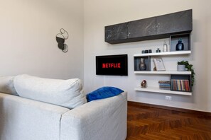 A living room with a grey sofa, a black TV mounted on the wall, and a bookshelf with various items. - Città Studi: Two-room apartment near the M2 Piola station (Milan)