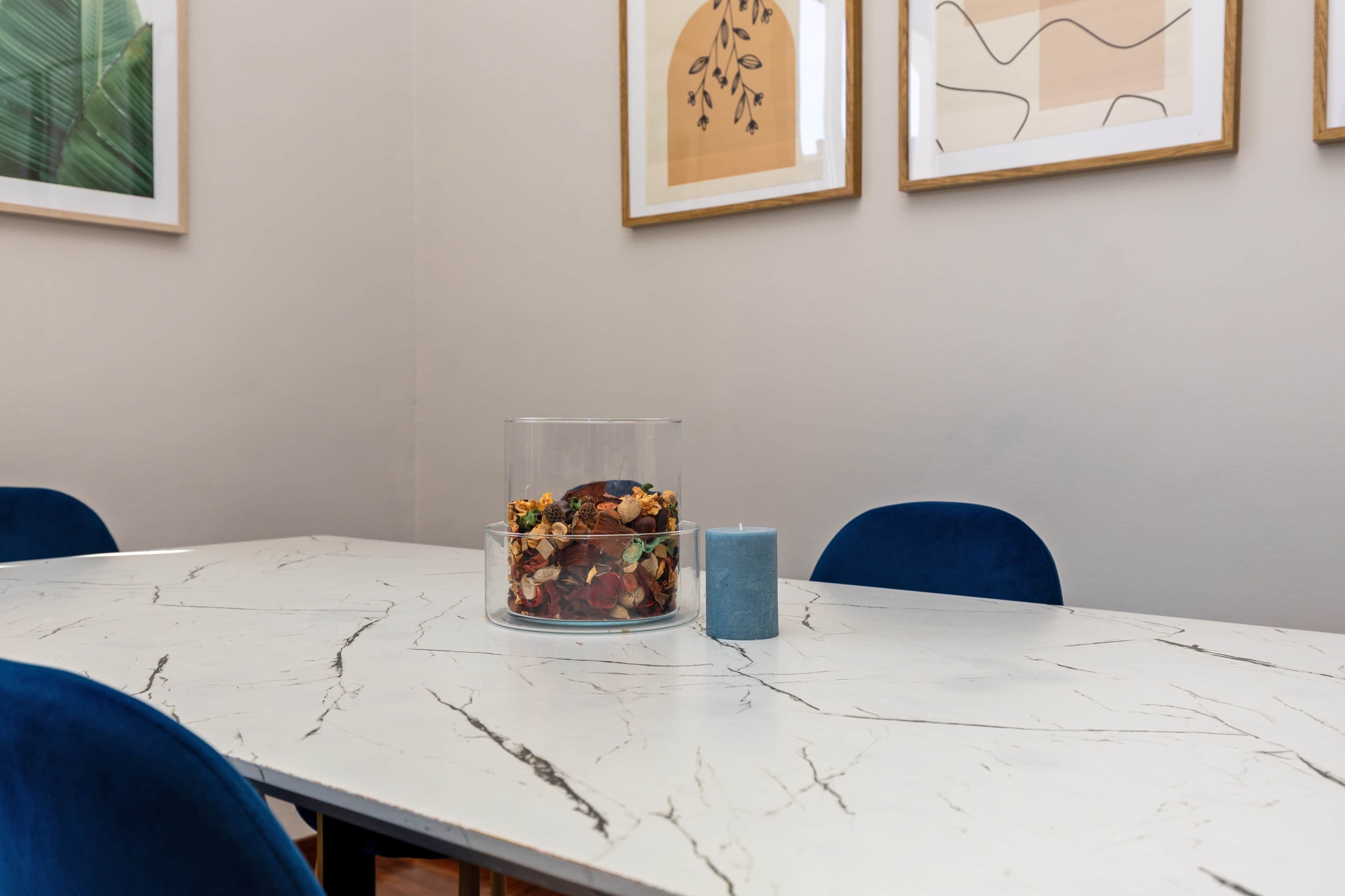 A dining table with a clear glass container filled with dried flowers and a blue candle.