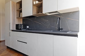 A modern kitchen with a black marble backsplash, a built-in microwave, and a sleek faucet. - Città Studi: Two-room apartment near the M2 Piola station (Milan)