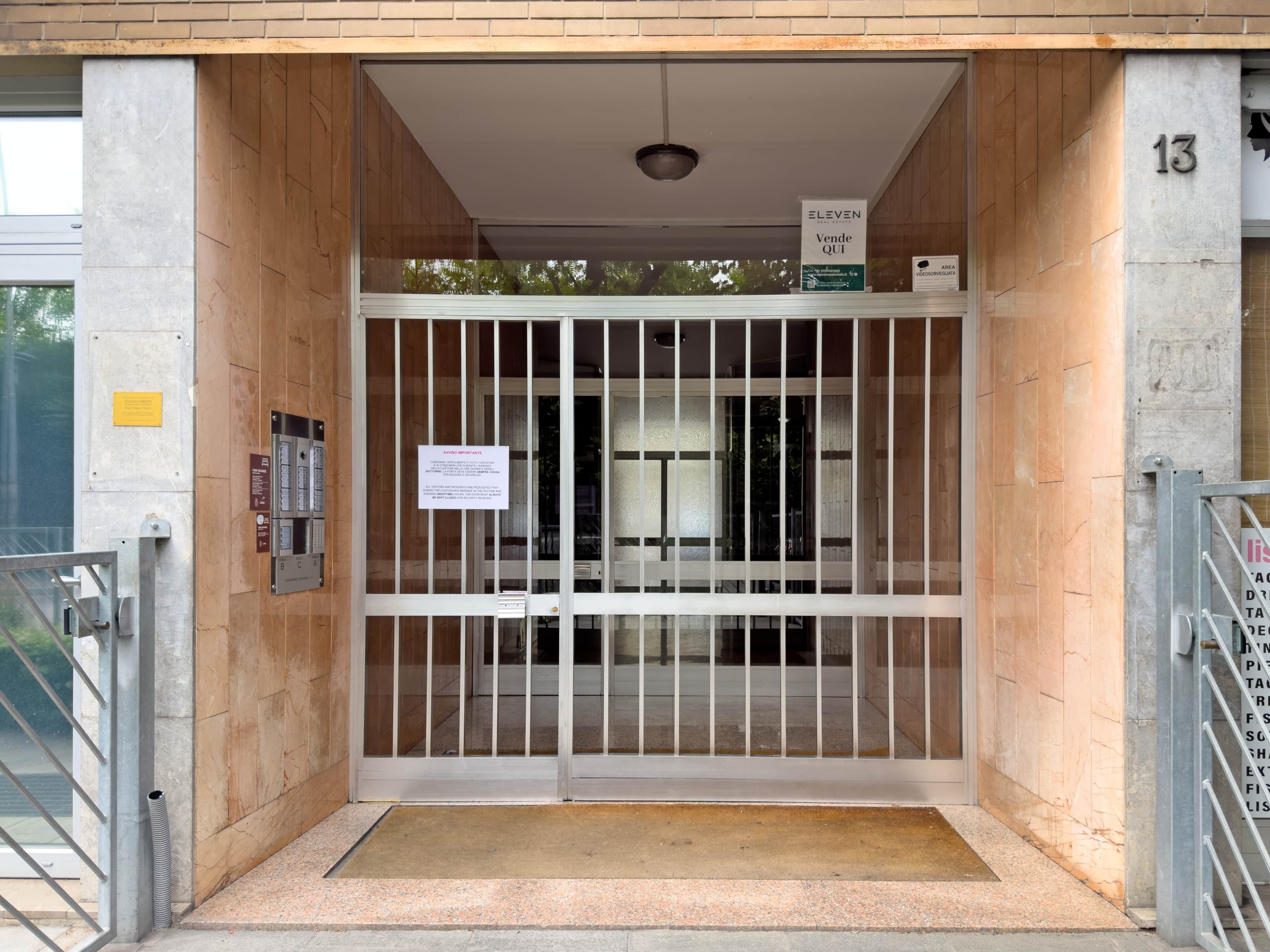 A gated entrance with a metal gate, a numbered column, and a sign above the gate.