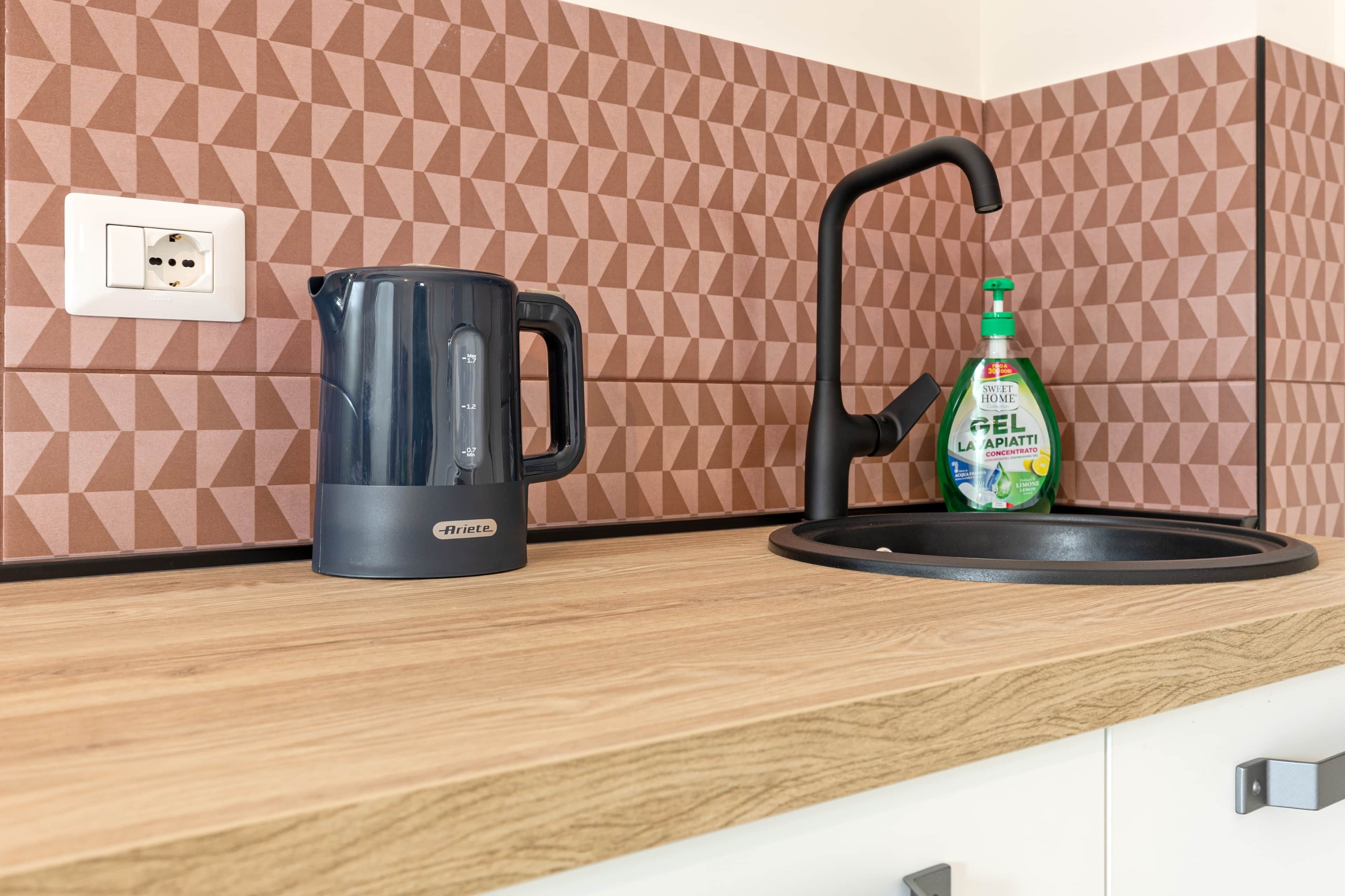 A kitchen with a coffee maker, a bottle of dish soap, and a power outlet on the wall.